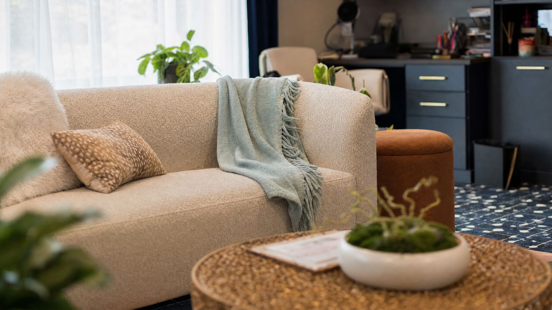 A cream sofa with a soft blue-green throw blanket and a speckled pillow beside a woven coffee table in Julia's office
